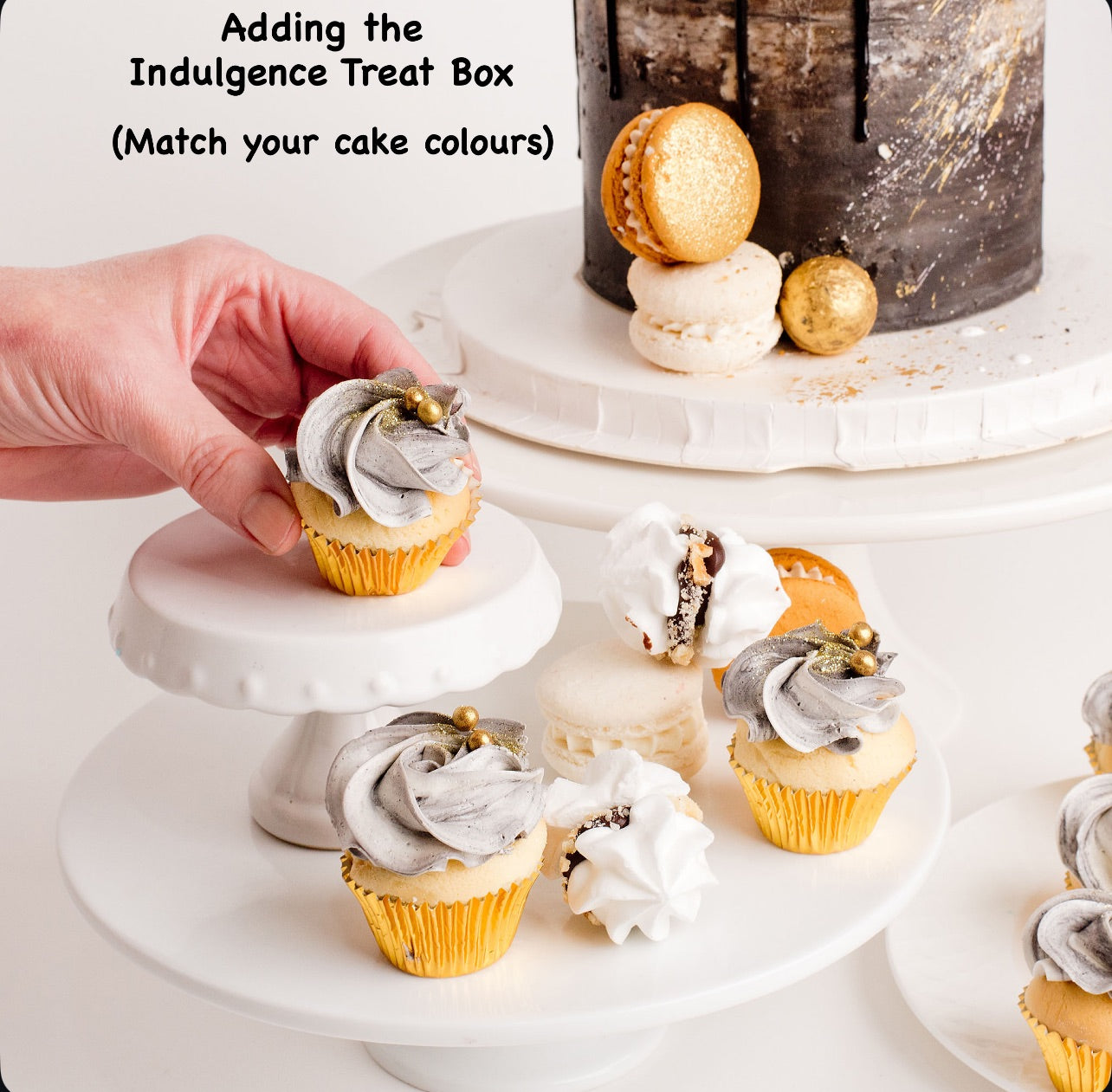 Decorative cupcakes with black and white frosting buttercream on a cake stand, with text about an Indulgence Treat Box.