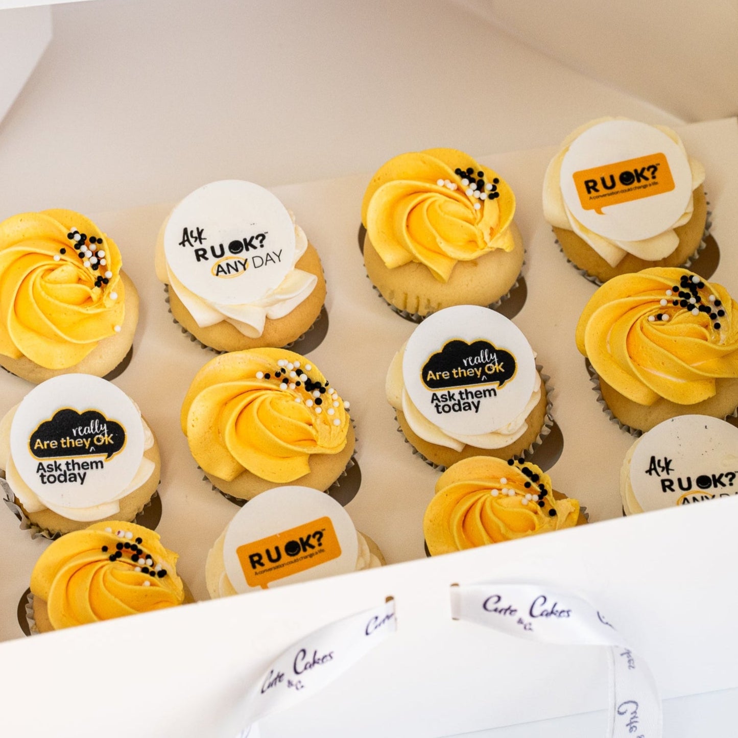 Mini cupcakes with yellow and white butterceam, some with black sprinkles and edible disks with 'R U OK?' text on them. RU Ok day, Cute Cakes and Co, Brisbane cake shop,