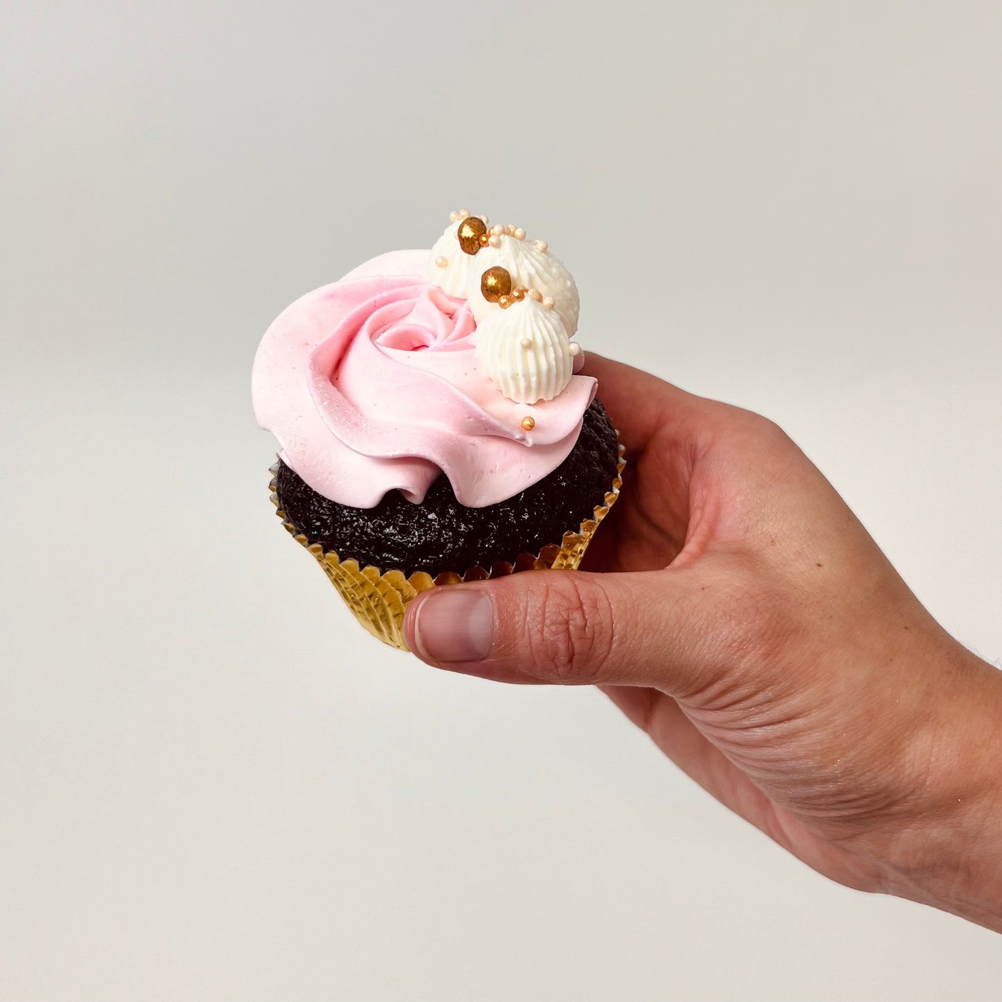 Hand holding a cupcake with light pink buttercream frosting and gold accents. Made by Cute Cakes and Co. Brisbane cake shop near you. Same day orders. We deliver to your door