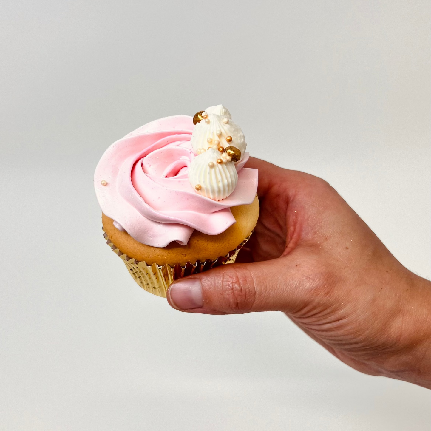 Holding a vanilla cupcake with pink buttercream frosting with white and gold detail. Made by Cute Cakes and Co. Brisbane cake shop near you. Same day orders. We deliver to your door