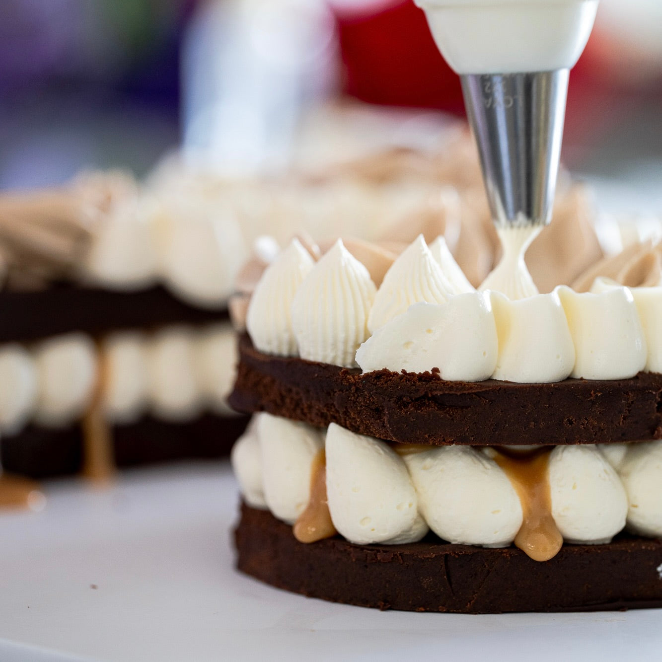 Close-up of a layered Dreamy number cake being piped with white buttercream and caramel sauce