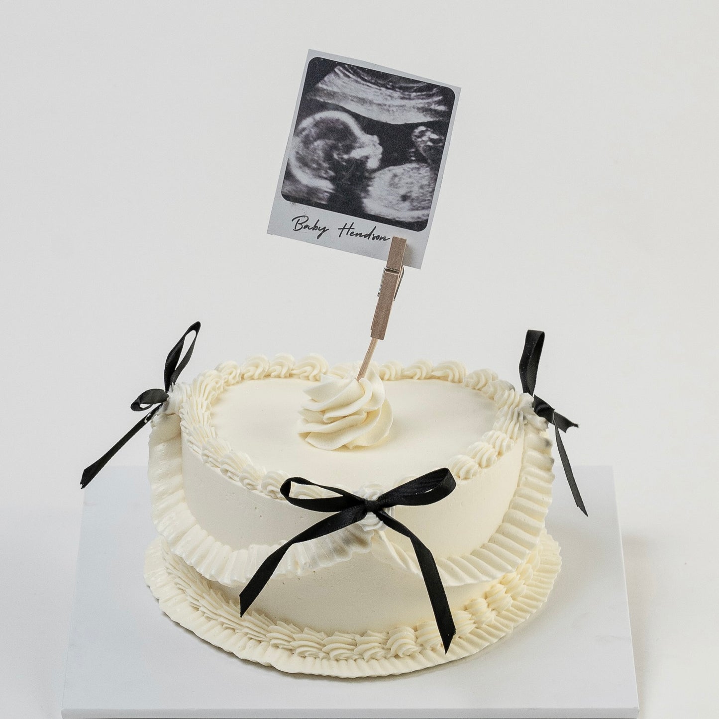 White Vintage style cake with black ribbons and a Polaroid photo ultrasound photo Perfect for baby announcement . Made with love by Cute Cakes and Co. the 5 star cake shop, in Brisbane.