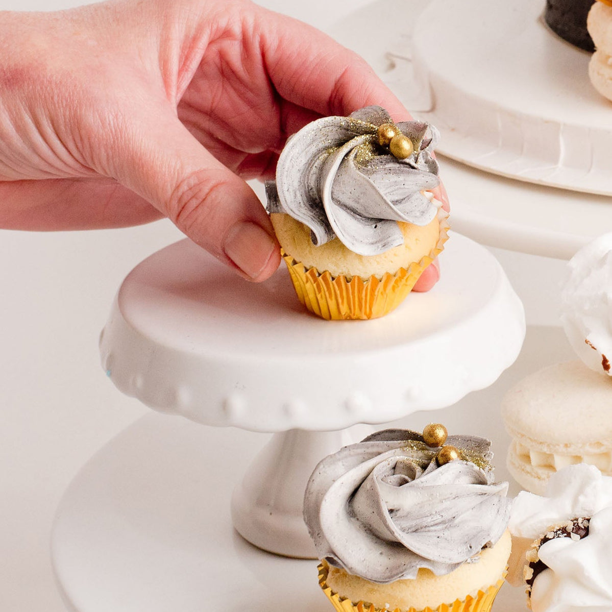 Delicious mini cupcakes with black and white buttercream, gold details on a white cake stand.