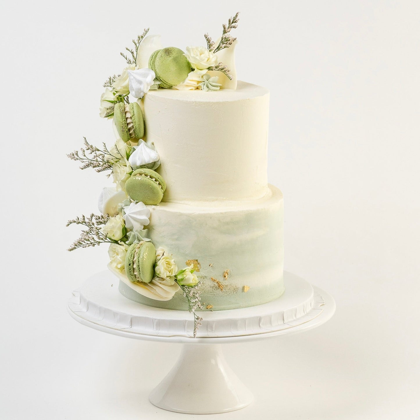 Two-tiered wedding cake with greenery and flowers on a white background