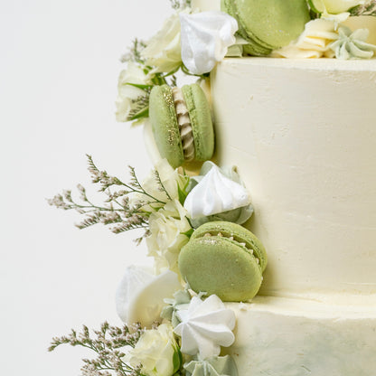 White cake with green macarons and white flowers on a light background