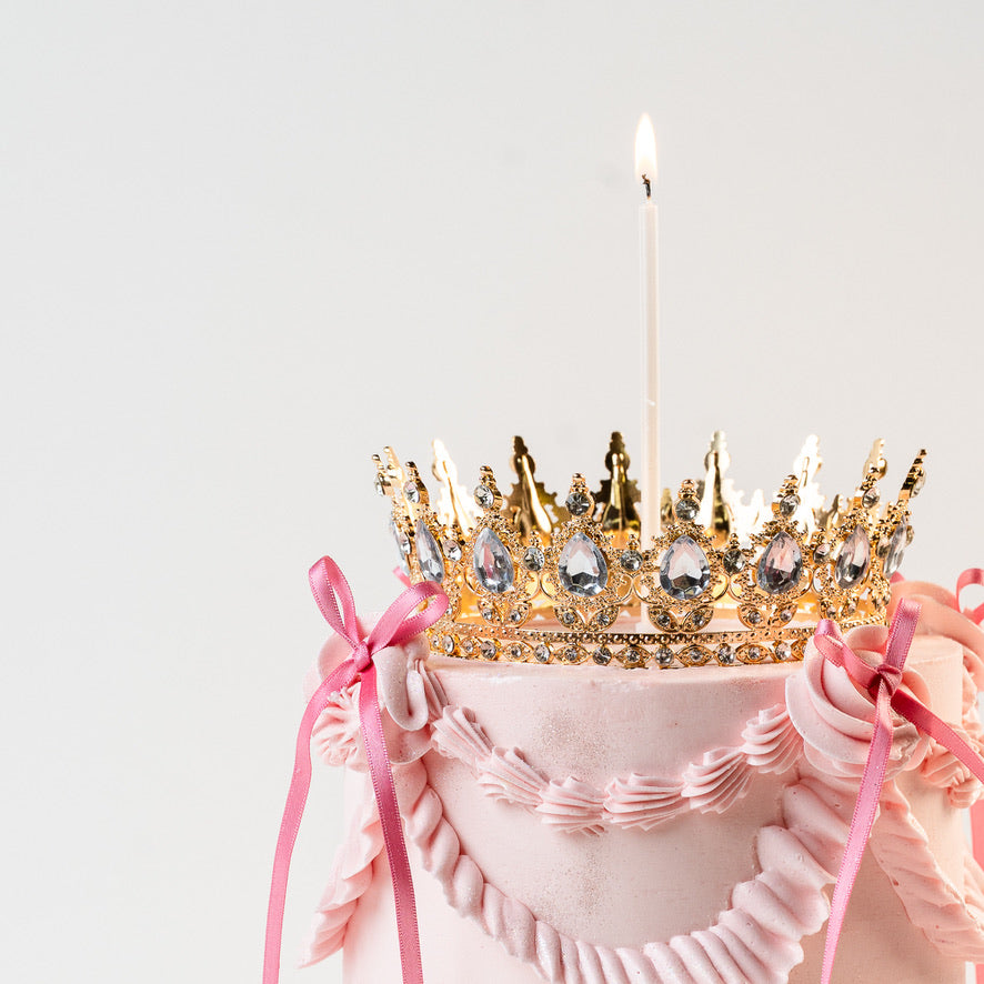 Close up of a vintage birthday cake with a gold crown topper. Lit candle