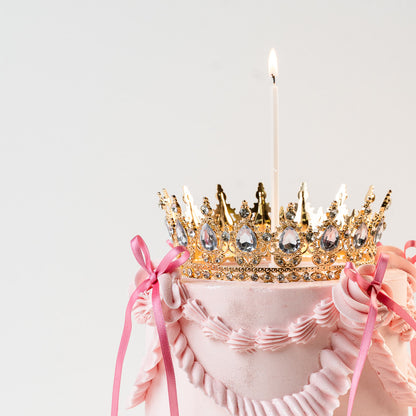 Close up of a vintage birthday cake with a gold crown topper. Lit candle