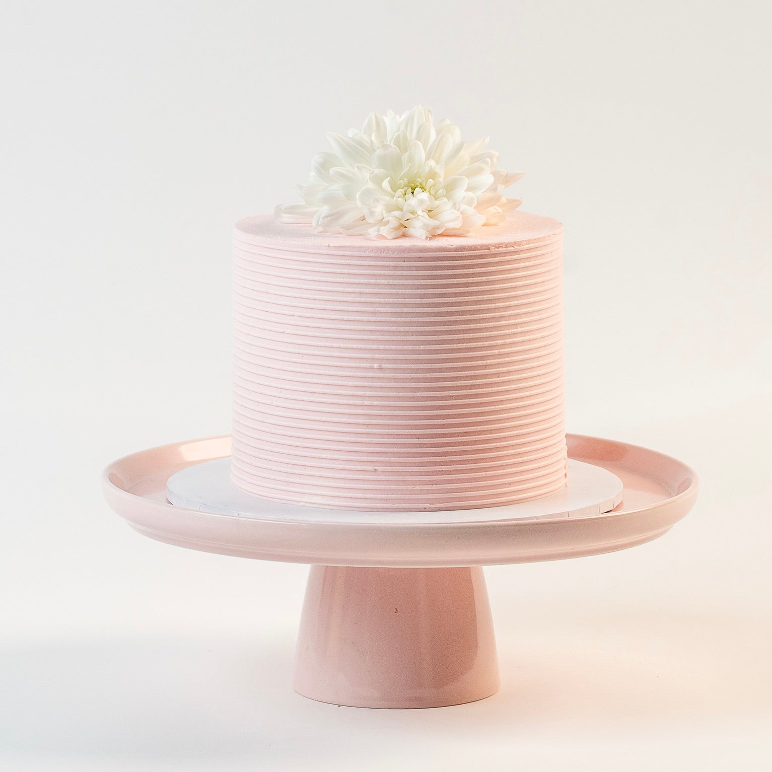 Light pink cake, decorated with ribbed buttercream feature on the sides and white fresh flowers on the top. Made with love by Brisbane’s favourite, 5 star cake shop, Cute Cakes & Co 