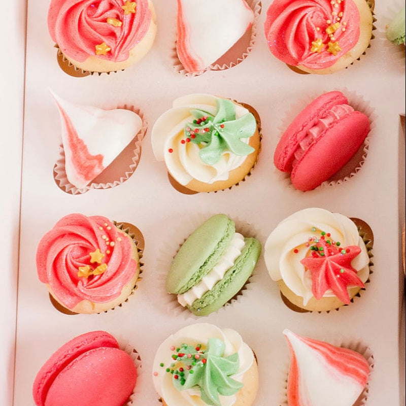 Assorted cupcakes and macarons in a box with red green, and white icing.