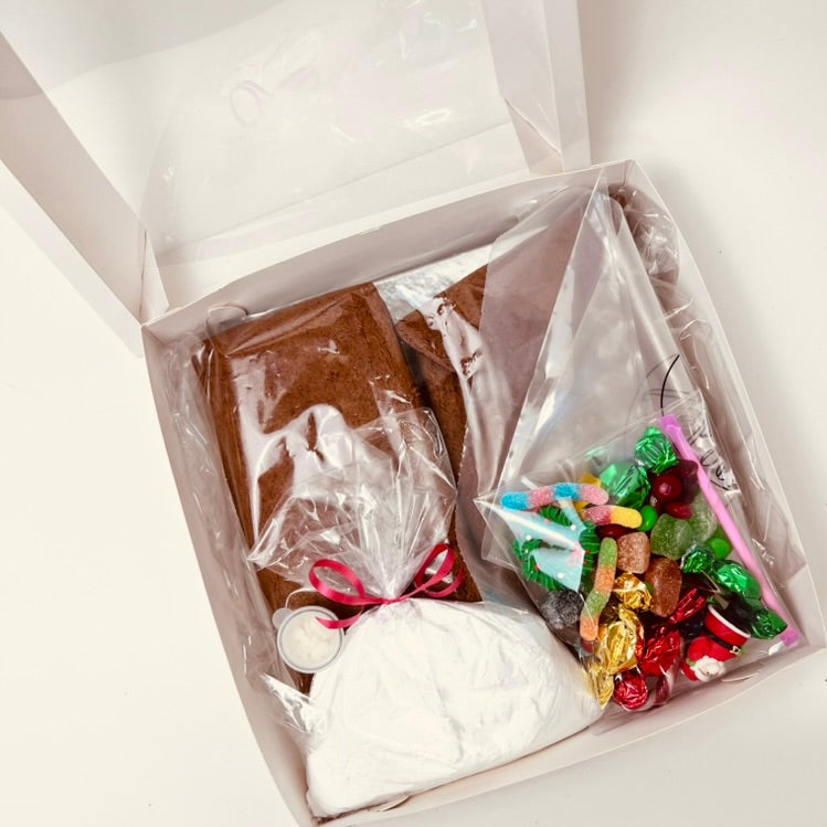Open gift box with gingerbread house, candy, and other items on a white background