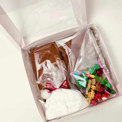 Open gift box with gingerbread house, candy, and other items on a white background