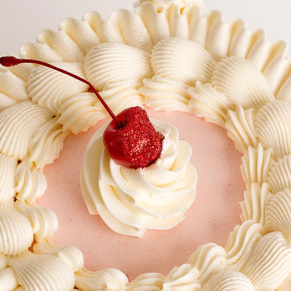 Close-up of a dessert with pink filling, white whipped cream, and a red cherry on top.