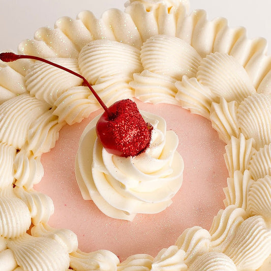 Close-up of a dessert with pink filling, white whipped cream, and a red cherry on top.