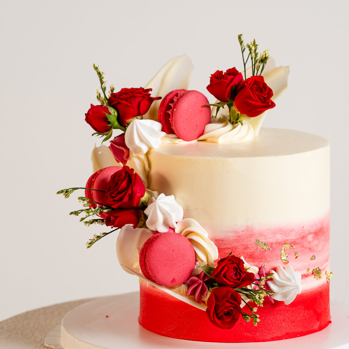 White & Red buttercream cake with cascade of macarons, fresh roses, white chocolate sails and gold leaf. 
