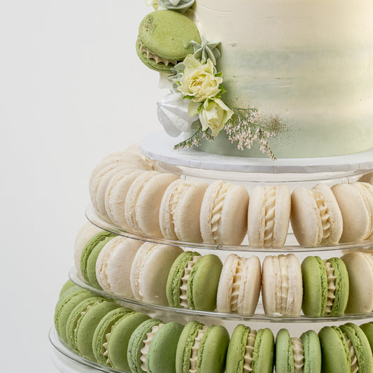 close up of white & green wedding cake with fresh flower  on a stand with white and green macarons. 