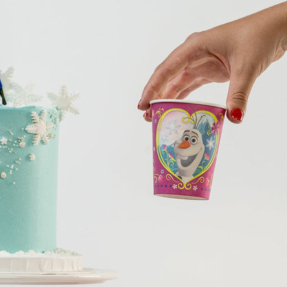 Blue cake with Elsa and Anna figurines and a hand holding a Frozen-themed cup.
