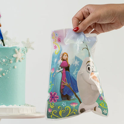 Cake with Frozen-themed decorations and a hand holding a matching bag on a white background