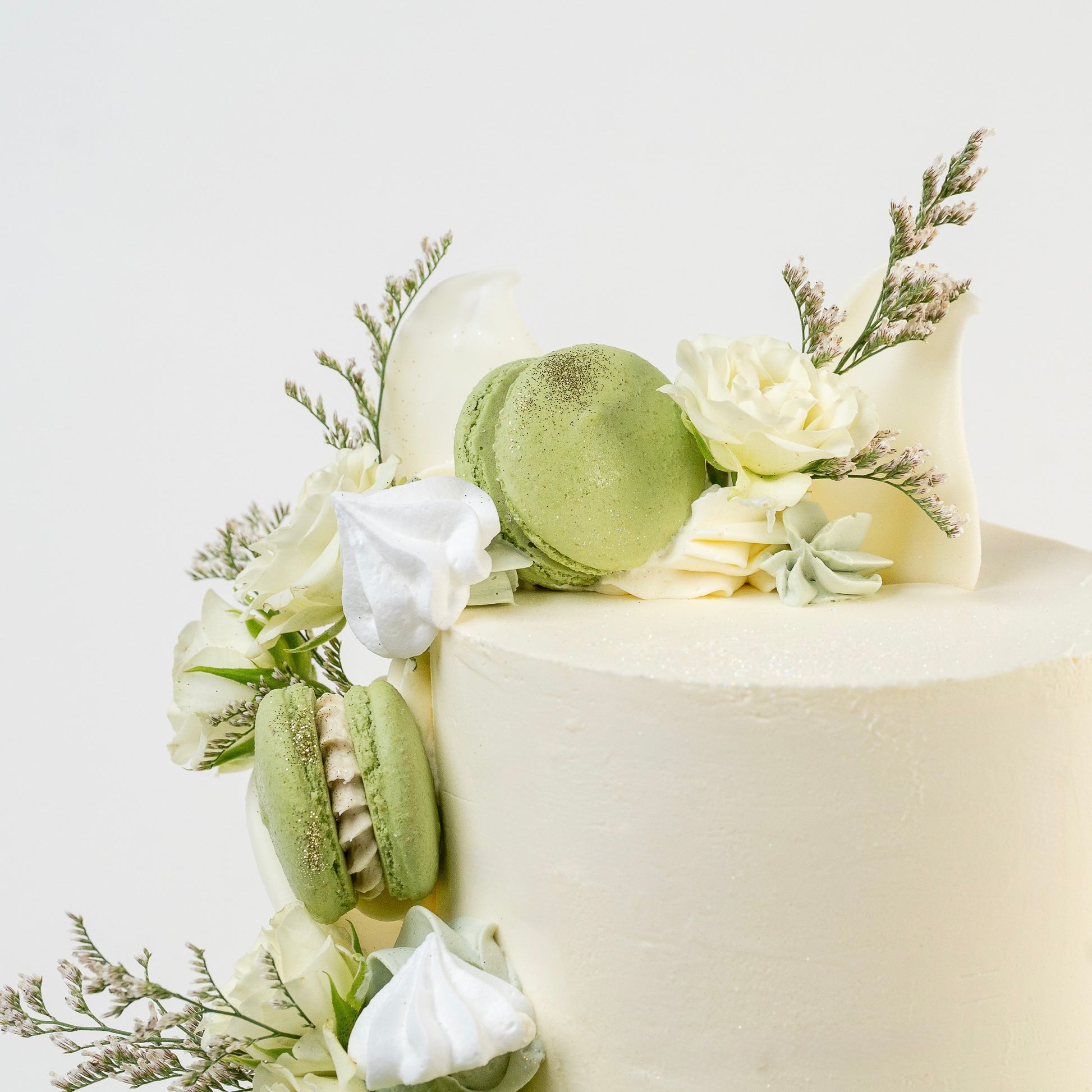 White cake with green macarons and white flowers on a light background