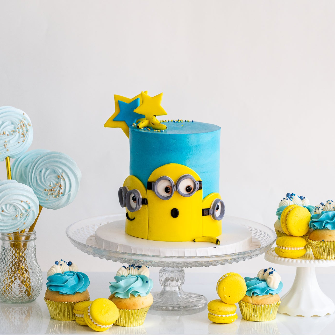 Minion birthday cake. Decorated with blue buttercream, three Despicable Me minions  characters on the front with icing bananas and stars as decoration. Also cupcakes, macaroons and other party decorations Looks fabulous, Made with love by the five star cake shop ,Cute Cakes and Co, Brisbane. 