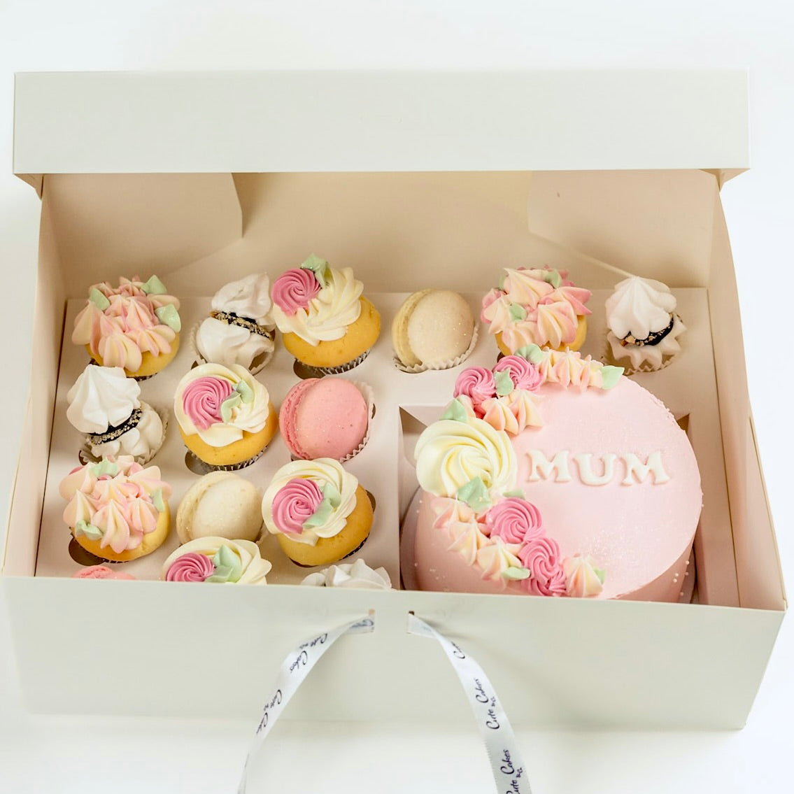 Decorative cake with 'MUM' on top, surrounded by smaller cupcakes in a box.
