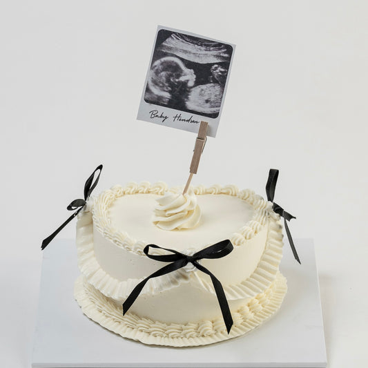 White Vintage style cake with black ribbons and a Polaroid photo photo Perfect for baby announcement . Made with love by Cute Cakes and Co. the 5 star cake shop, in Brisbane.