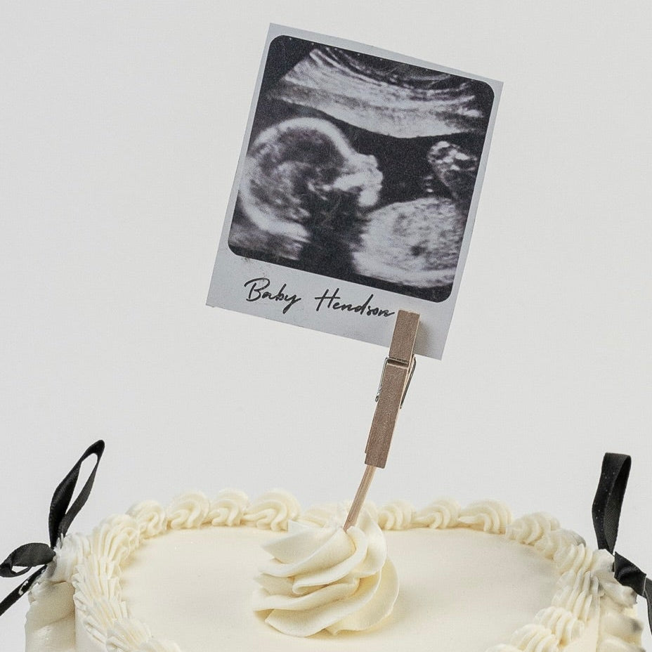 White Vintage style cake with black ribbons and a Polaroid photo photo Perfect for baby announcement . Made with love by Cute Cakes and Co. the 5 star cake shop, in Brisbane.