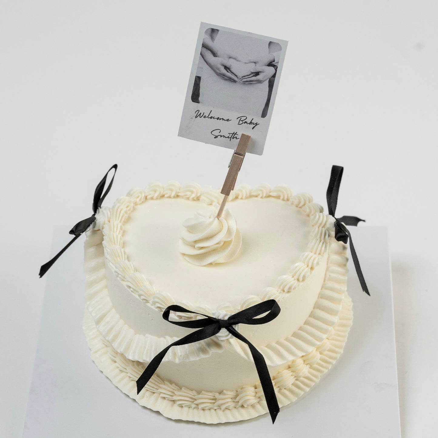 White Vintage style cake with black ribbons and a Polaroid photo photo Perfect for baby announcement . Made with love by Cute Cakes and Co. the 5 star cake shop, in Brisbane.
