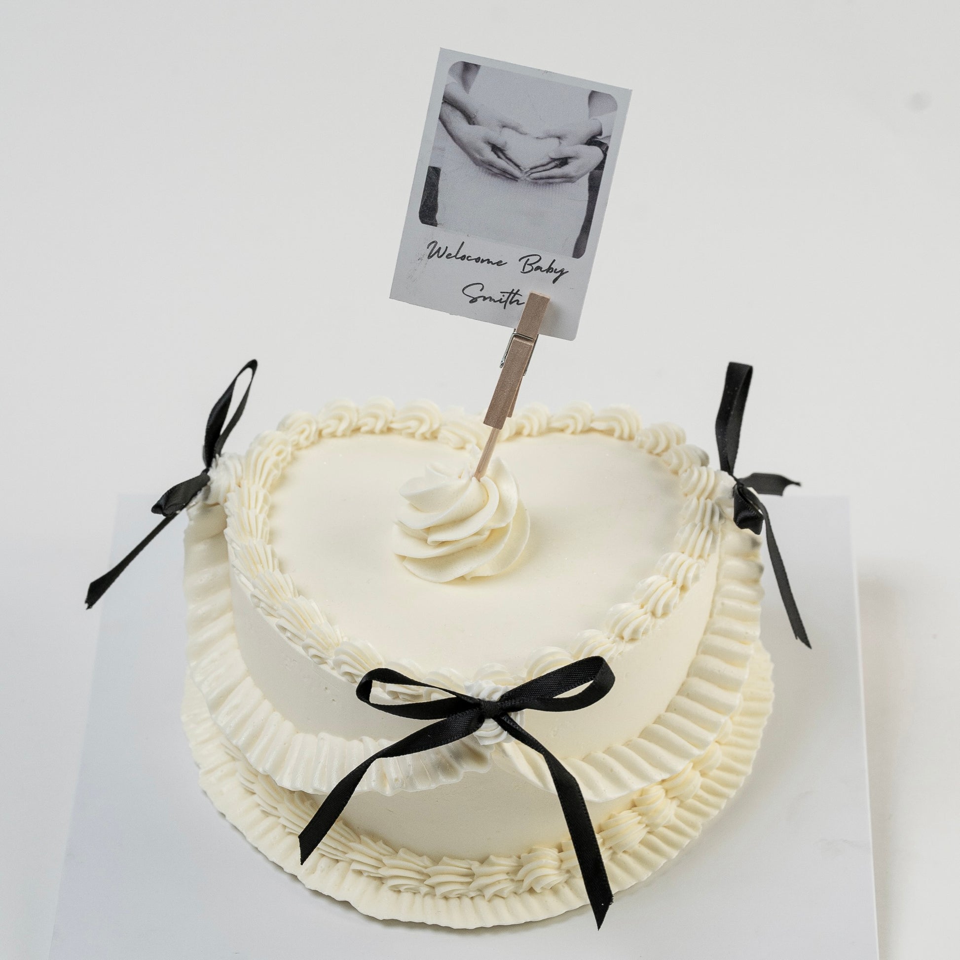 White Vintage style cake with black ribbons and a Polaroid photo photo Perfect for baby announcement . Made with love by Cute Cakes and Co. the 5 star cake shop, in Brisbane.