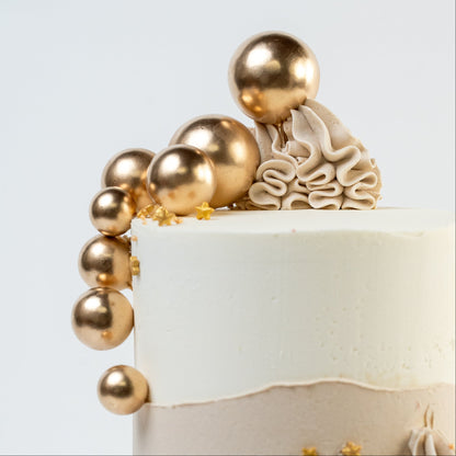 Close up shoot of white and caramel cake with gold balls and stars. Wiggle of buttercream at base and white Macaron. For perfect for engagements baby shower birthdays Looks fabulous, Made with love by Cute Cakes and Co. the 5 star review cake shop, in Brisbane.