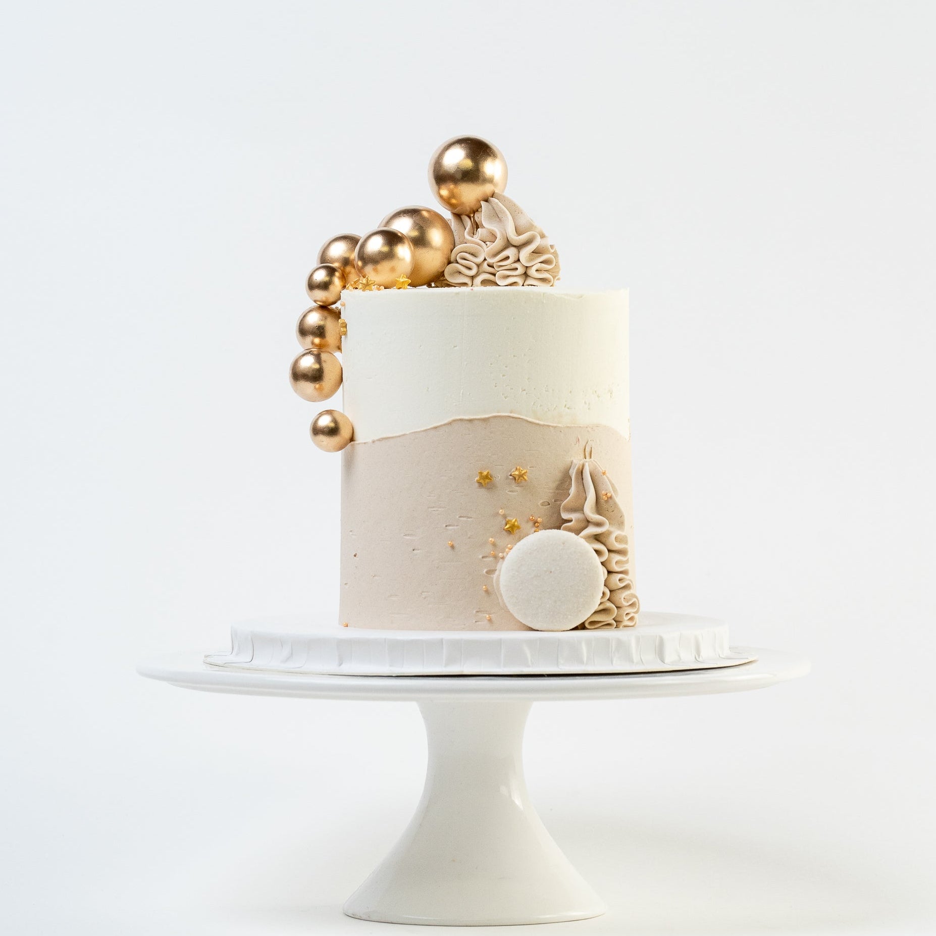 White, caramel cake with gold balls and stars. Wiggle of buttercream at base and white Macaron. For perfect for engagements baby shower birthdays Looks fabulous, Made with love by Cute Cakes and Co. the 5 star review cake shop, in Brisbane.