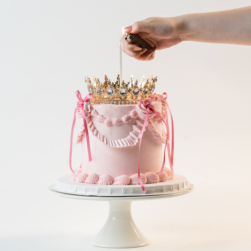 Candle being lit on a Pink Vintage style birthday cake. Pink ribbon bow with a gold crown on the top and candle. Made with love by Brisbane’s favourite, 5 star cake shop, Cute Cakes & Co 