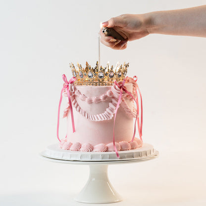 Candle being lit on a Pink Vintage style birthday cake. Pink ribbon bow with a gold crown on the top and candle. Made with love by Brisbane’s favourite, 5 star cake shop, Cute Cakes & Co 