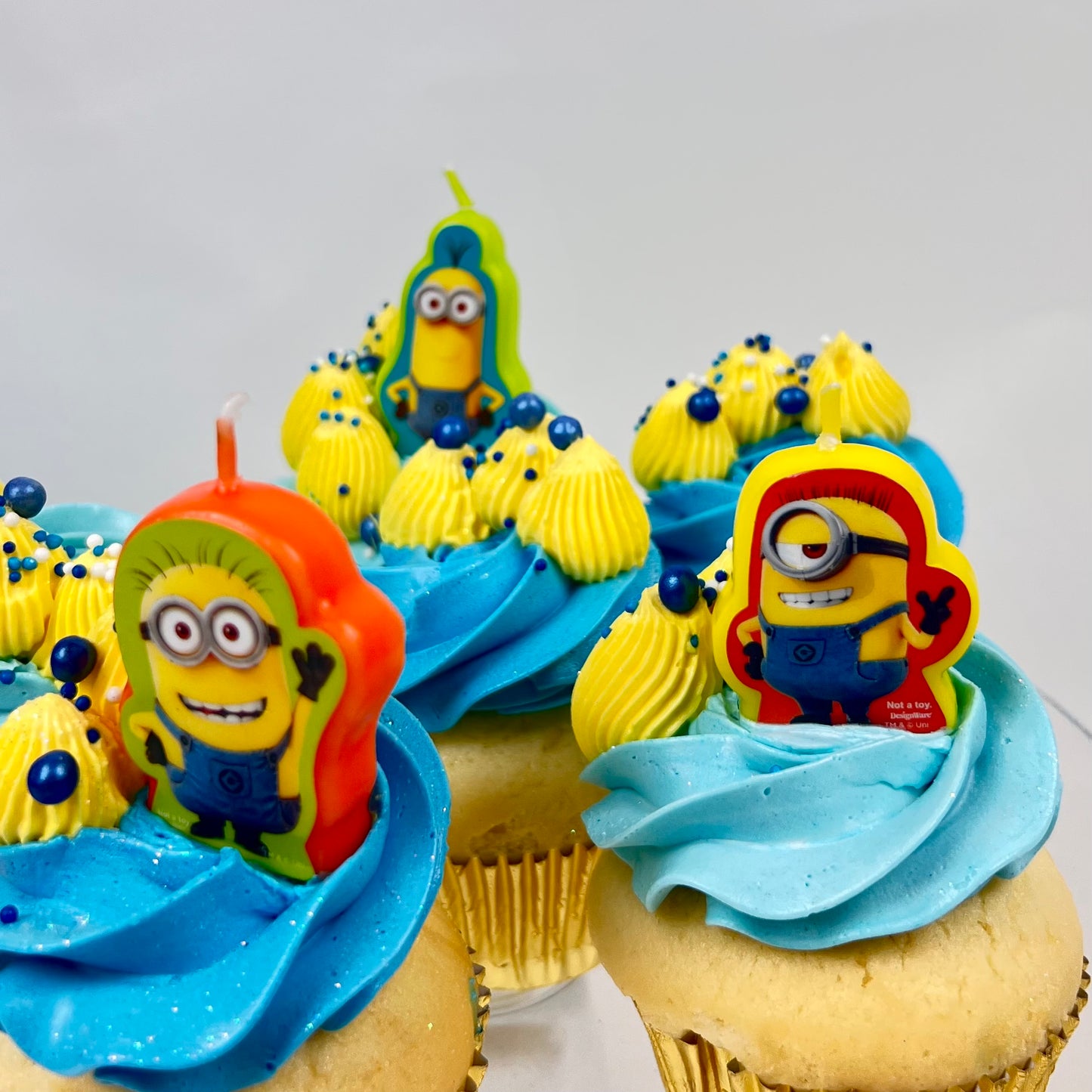Cupcakes with blue frosting and Minion-themed candles on a white background