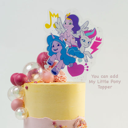 Hands placing down a My little pony cake topper on the top of  Pretty pink and yellow cake with a side decoration of shades of pink and clear balls. Wiggle and yellow macaron at the base. glitter perfect for a  girl's birthday Looks fabulous.  Made with love by Cute Cakes & Co, Brisbane Favourite cake shop. 
5 star review cake shop in Brisbane. 