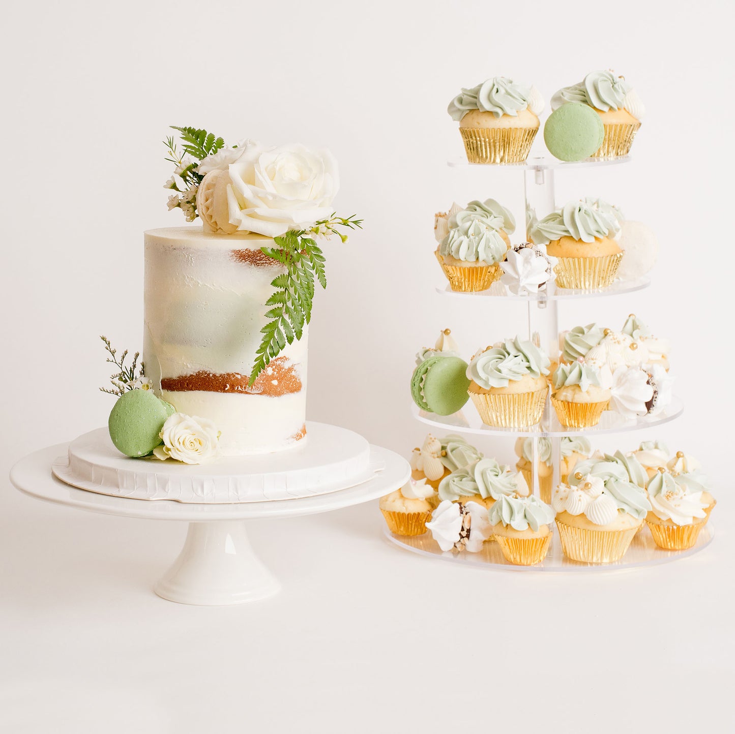 White cake with fresh flowers and a cupcake stand . All in sage green adn white Looks fabulous, Made with love by Cute Cakes and Co. the 5 star review cake shop, in Brisbane.