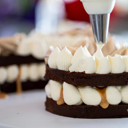 Close-up of a layered Dreamy number cake being piped with white buttercream and caramel sauce