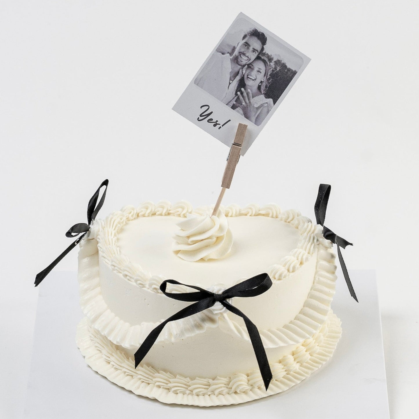 White Vintage style cake with black ribbons and a Polaroid photo on a white background. Perfect for engagements. Made with love by Cute Cakes and Co. the 5 star cake shop, in Brisbane.