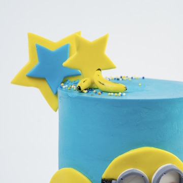 top shoot of Minion birthday cake. Decorated with blue buttercream, three Despicable Me minions  characters on the front with icing bananas and stars as decoration.  Looks fabulous, Made with love by the five star cake shop ,Cute Cakes and Co, Brisbane. 