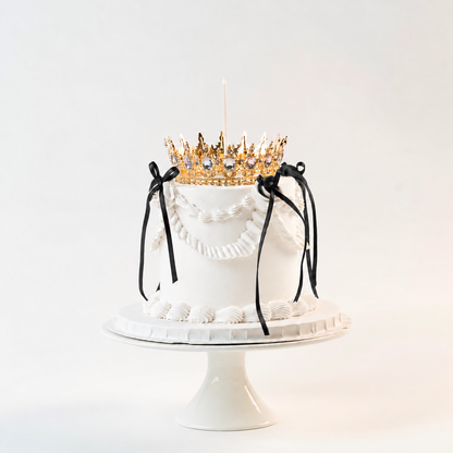 White Vintage style birthday cake. Black ribbon bow with a crown on the top and candle.