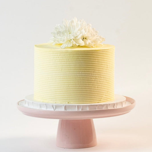 Light sherbet yellow colour cake, decorated with ribbed buttercream feature on the sides and white fresh flowers on the top. 