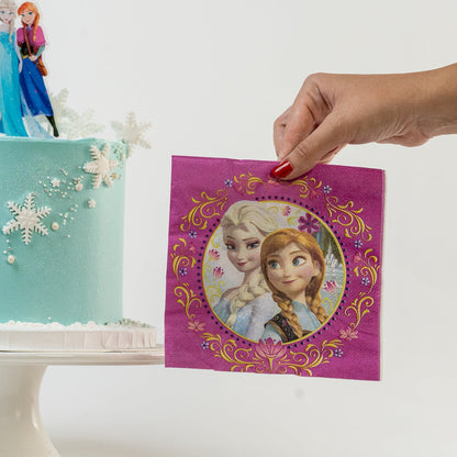 Frozen-themed cake with Elsa and Anna figurines and a hand holding a matching serviette