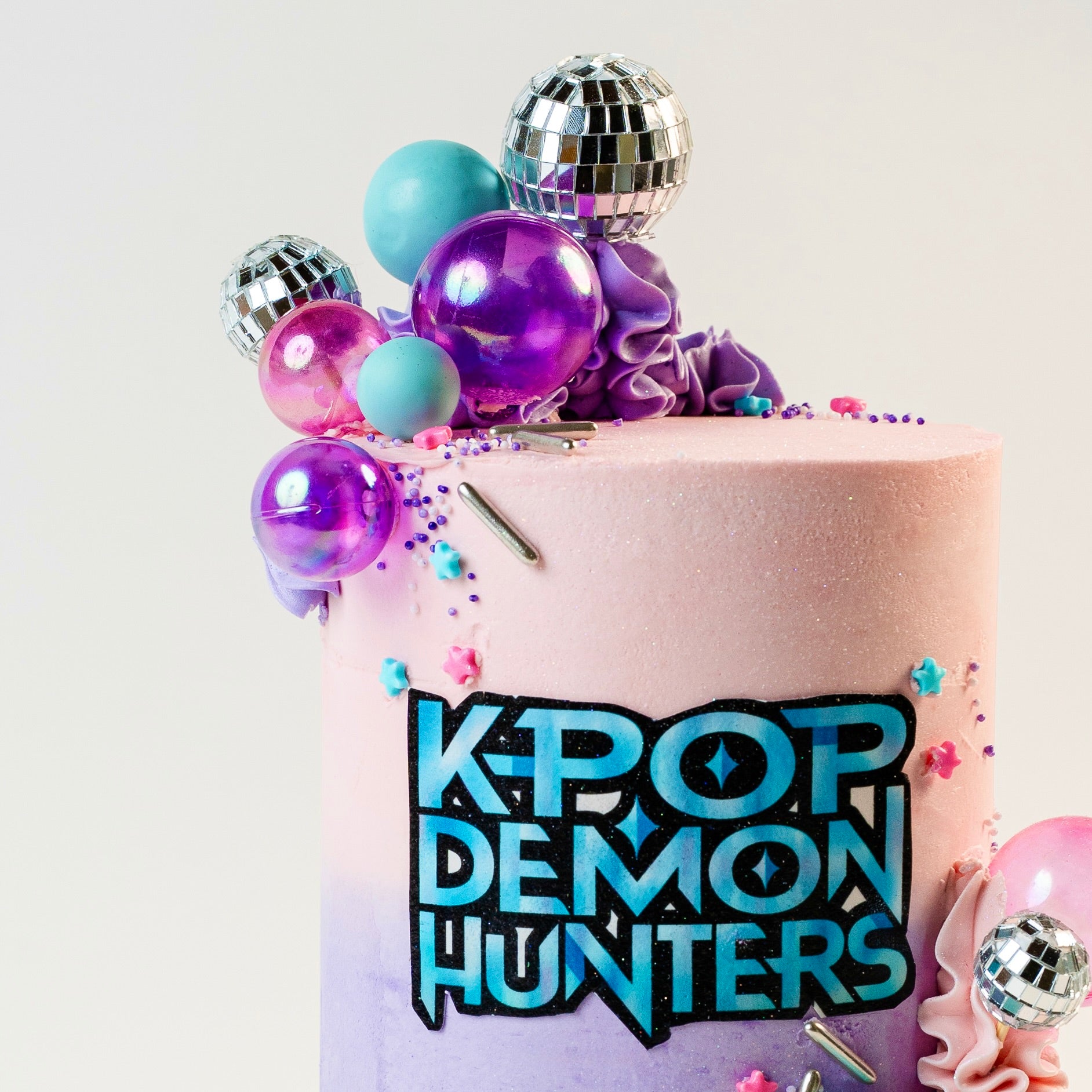 K-pop Demon Hunters birthday cake. 
Pink, Blue and purple buttercream and decorations. With disco balls. K-Pop Demon Hunters logo at the front. Made with love by Brisbane’s favourite, 5 star cake shop, Cute Cakes & Co 