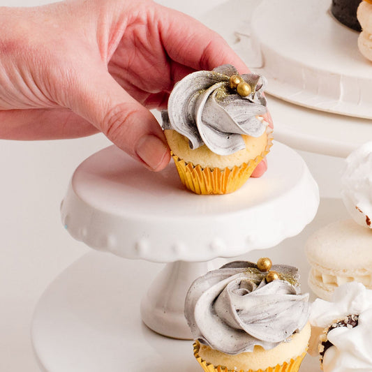 Delicious mini cupcakes with black and white buttercream, gold details on a white cake stand.