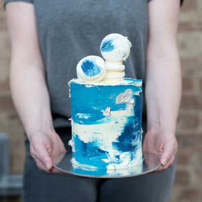 Blue artistic buttercream cake with white macarons and silver details